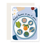 A Passover card featuring a vibrant illustration of a traditional seder plate adorned with symbolic Passover foods, including matzo, bitter herbs, charoset, and an egg, accompanied by the text "Happy Passover to you and yours."