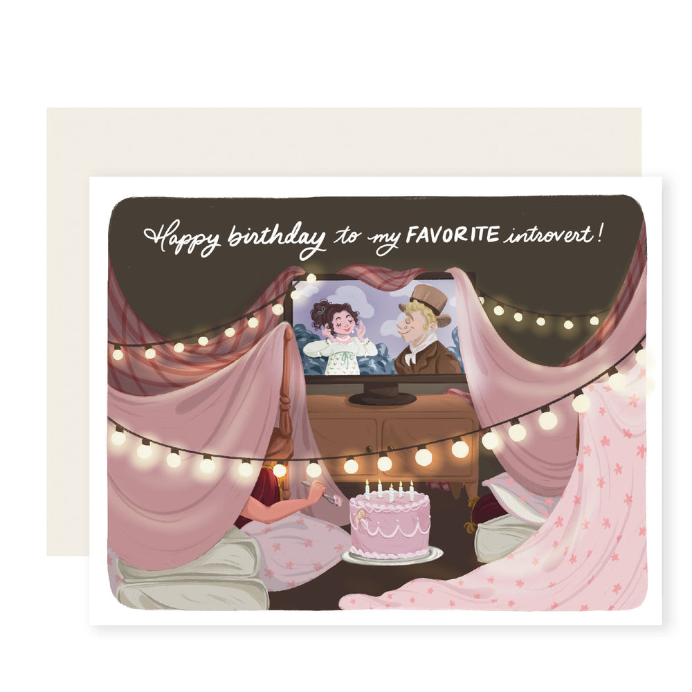 A charming birthday card with an illustration of a cozy blanket fort adorned with twinkling lights. In the background, a movie plays, setting a cozy atmosphere. A figure inside the fort enjoys a cake. The card reads, 'Happy Birthday to my favorite introvert,' capturing the warmth and celebration of a special day in a unique and intimate setting.