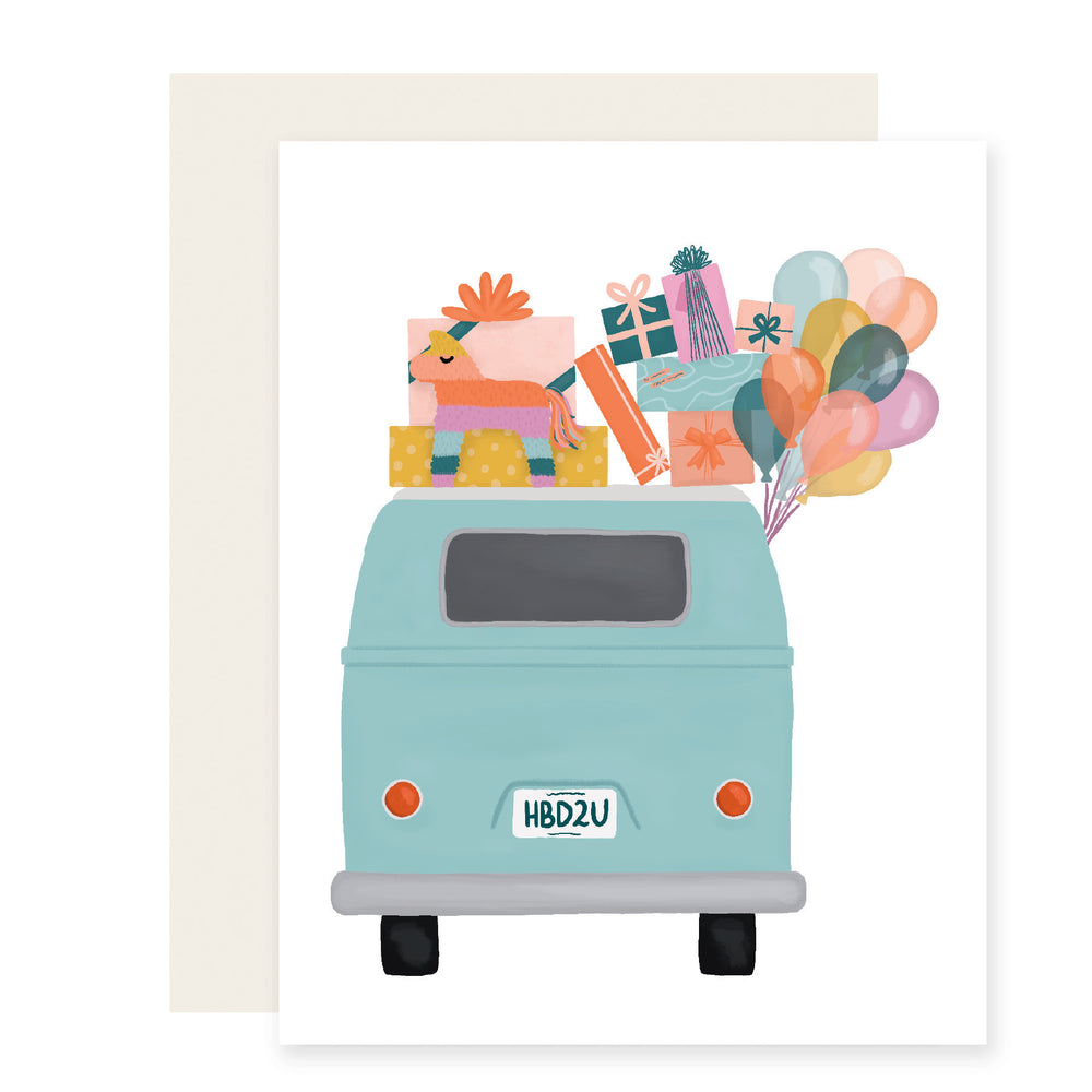 An adorably illustrated birthday card featuring a light blue VW bus with the license plate reading 'HB2U' (Happy Birthday to You). The top of the van is adorned with a joyful pile of colorful balloons and presents, adding a whimsical touch to the celebratory scene.