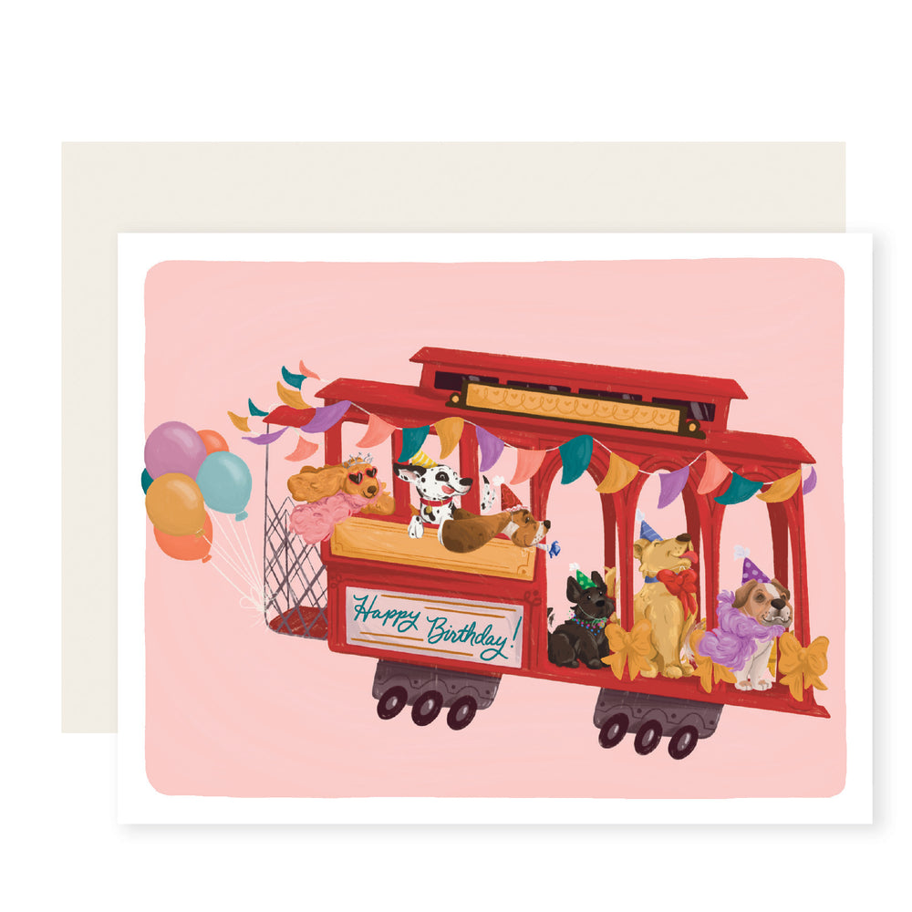 Dogs in party hats ride a festive red cable car in a birthday card illustration. The card reads 'Happy Birthday,' adding whimsy and joy for dog lovers and celebration enthusiasts.