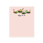 A light pink notepad featuring adorable frog and lily pad illustrations at the top. The notepad's header humorously reads 'Hop to it.' This playful notepad is perfect for adding a touch of whimsy to your notes and tasks.
