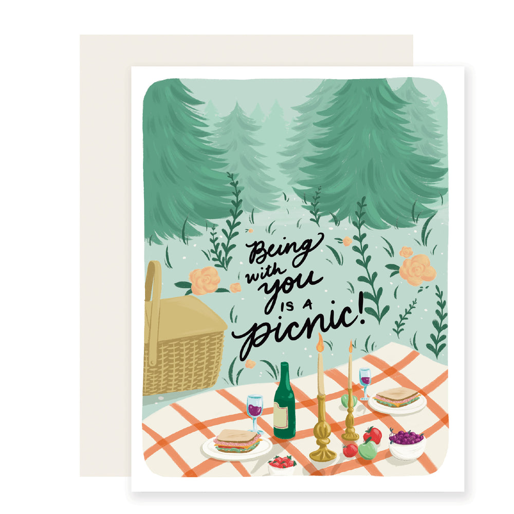 A love card featuring the text 'Being with you is a picnic' against a beautifully illustrated picnic scene set in an evergreen forest. The card displays an idyllic picnic layout in a serene natural setting.