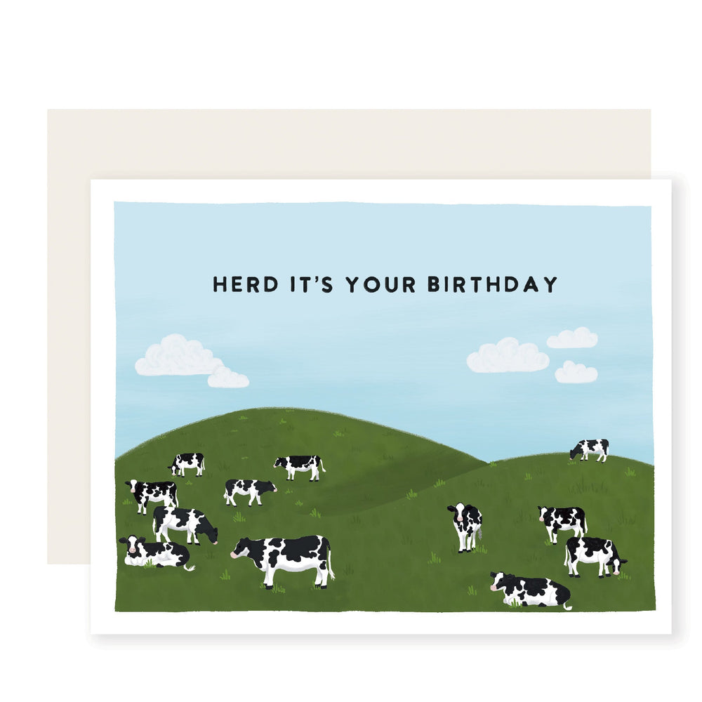 A whimsically illustrated birthday card featuring a picturesque pasture with a cheerful herd of cows. The card playfully reads, 'Herd it's your birthday,' making it a perfect choice for a pun-loving friend.