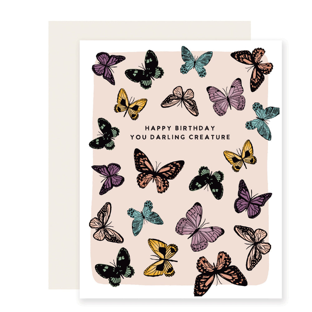 A birthday card with a pink backdrop featuring the message 'Happy Birthday, you darling creature,' adorned with beautifully illustrated multicolored butterflies, creating a whimsical and enchanting design.