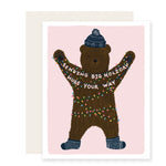 An endearing holiday card with an adorably  illustrated bear wrapped in holiday lights and wearing a cozy knit winter hat and socks. The bear holds a banner that reads Sending big holiday hugs your way adding a heartwarming touch to the festive scene