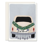 A wedding card featuring an adorable illustration of a car with a 'Just Married' banner on the back. The car is adorned with beautiful green garlands and cans, symbolizing the joy and celebration of the newlyweds.